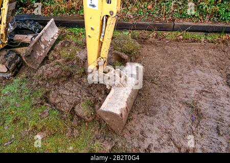 Cardiff, PAYS DE GALLES - JANVIER 2020: Gros plan du godet d'une mini pelle hydraulique creusant la pelouse dans le jardin arrière d'une propriété résidentielle Banque D'Images