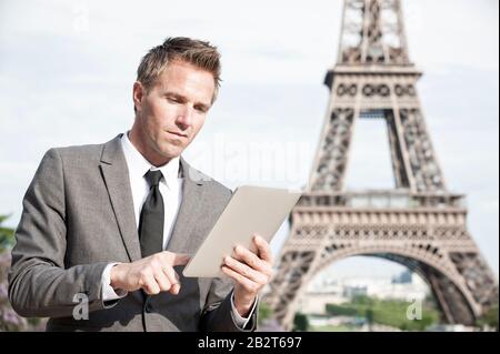 Homme d'affaires européen utilisant une tablette à l'extérieur devant la Tour Eiffel à Paris, France Banque D'Images