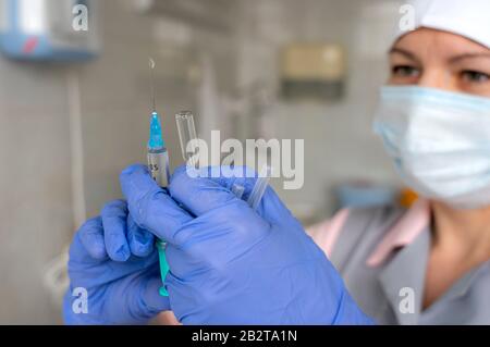 l'infirmière médicale se rapproche en gants bleus avec une seringue dans les mains se préparant à donner une injection. Banque D'Images
