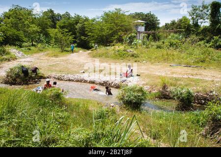 Femme se lavant des vêtements sur la rivière, enfants jouant dans l'eau, derrière une base déserte de l'ONU, mission de paix casque bleu Minustah, Mission des Nations Banque D'Images