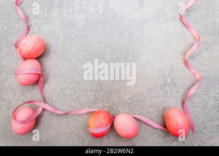 Oeufs roses (rosés) de Pâques avec des rubans de pois de polka en satin en rayons ensoleillés. Sur fond de pierre. Cadre, vue de dessus. Banque D'Images