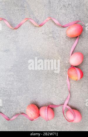 Oeufs roses (rosés) de Pâques avec des rubans de pois de polka en satin en rayons ensoleillés. Sur fond de pierre. Cadre, vue de dessus. Banque D'Images