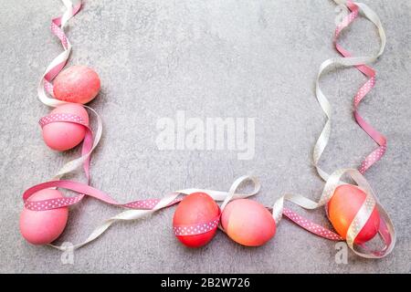 Oeufs roses (rosés) de Pâques avec des rubans de pois de polka en satin en rayons ensoleillés. Sur fond de pierre. Cadre. Banque D'Images