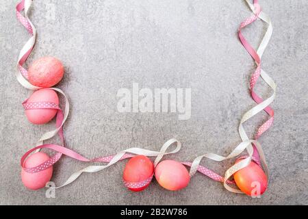 Oeufs roses (rosés) de Pâques avec des rubans de pois de polka en satin en rayons ensoleillés. Sur fond de pierre. Cadre, vue de dessus. Banque D'Images