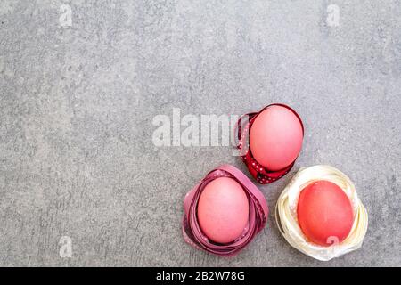 Œufs roses (rosés) de Pâques dans les nids de ruban en satin à pois de polka. Sur fond de pierre en rayons ensoleillés, vue de dessus. Banque D'Images