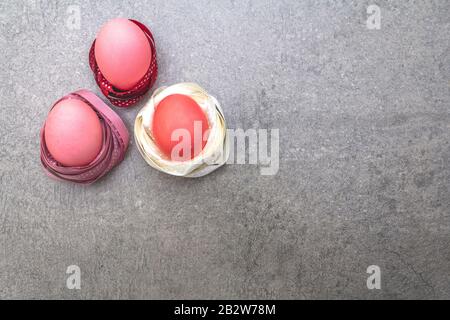 Œufs roses (rosés) de Pâques dans les nids de ruban en satin à pois de polka. Sur fond de pierre en rayons ensoleillés, vue de dessus. Banque D'Images