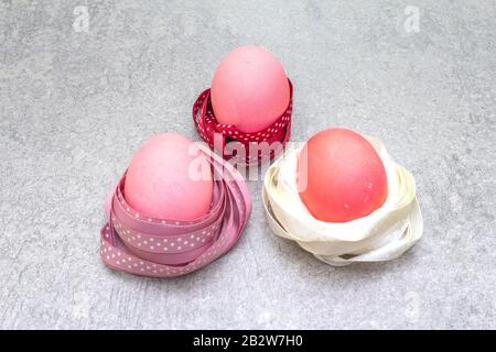 Œufs roses (rosés) de Pâques dans les nids de ruban en satin à pois de polka. Sur fond de pierre en rayons ensoleillés. Banque D'Images