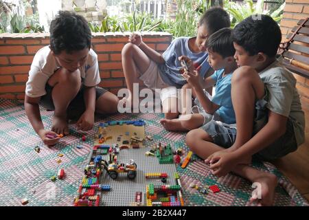 Un groupe d'enfants jouent au jouet Lego alors que l'un d'eux joue au jeu sur un smartphone. Banque D'Images