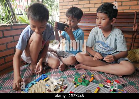 Un groupe d'enfants jouent au jouet Lego alors que l'un d'eux joue au jeu sur un smartphone. Banque D'Images