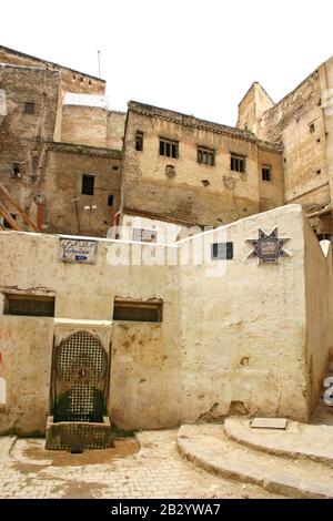 Fontaine d'eau, maisons et panneaux sur une rue résidentielle typique dans l'ancienne médina, Fes el Bali, à Fès, au Maroc. Banque D'Images