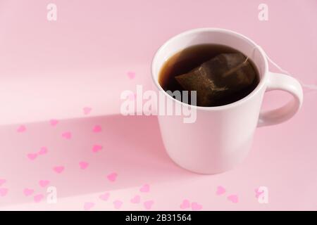 Tasse rose avec thé noir chaud sur fond rose avec coeurs de papier dispersés. Concept d'amour et de soins. Espace de copie pour le texte. Banque D'Images