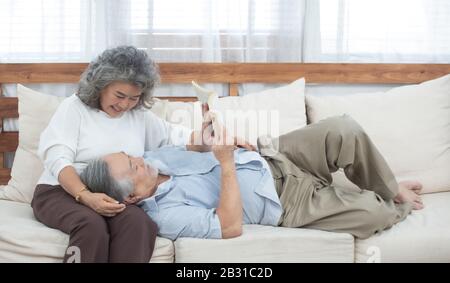 L'homme asiatique aîné senior se trouve sur le canapé lire livre avec grand-mère dans le salon à la maison. Banque D'Images