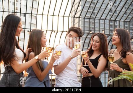 Groupe de plusieurs hommes asiatiques tenant un verre de vin discuter avec des amis tout en célébrant la fête de danse sur le toit de la discothèque extérieure. Banque D'Images