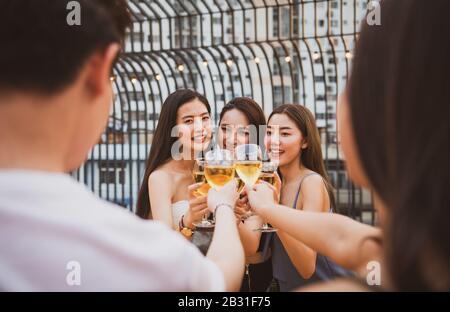 Un groupe de jeunes femmes asiatiques heureux et joyeux tenant un verre de vin discuter avec des amis tout en célébrant la fête de danse sur le toit de la discothèque extérieure Banque D'Images