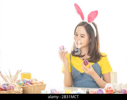 Belle jeune femme asiatique qui peint des œufs de pâques sur table avec des œufs décorés pour célébrer le jour de Pâques d'avril avec espace de copie. Banque D'Images