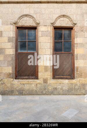 Façade de vieux mur de briques en pierre abandonné avec deux fenêtres d'obturation en bois voûtées adjacentes Banque D'Images