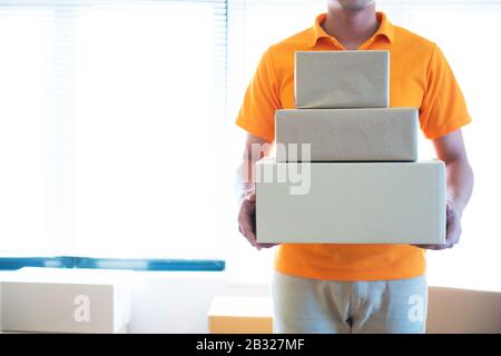 Livraison jeune homme asiatique en uniforme tenant et transportant pile de carton postel au bureau. Banque D'Images