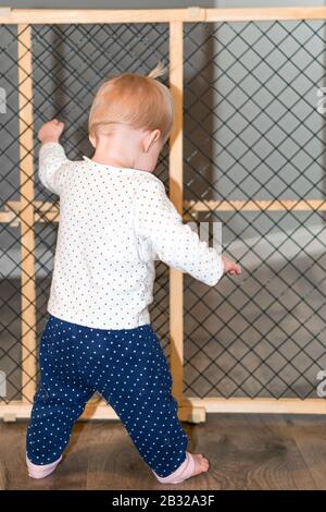 Bébé Mignon Debout À Côté De La Porte De Sécurité À La Maison Banque D'Images