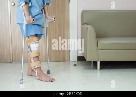 Patient asiatique avec renfort de genou avec bâton de marche et soutien de genouillères dans le service hospitalier après la chirurgie du ligament. Banque D'Images