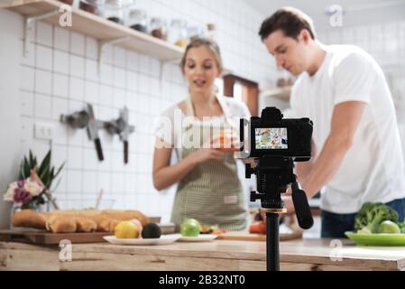 Appareil photo numérique professionnel sans miroir enregistrement vidéo blog de heureux caucasien couple cuisine dans la salle de cuisine. Banque D'Images