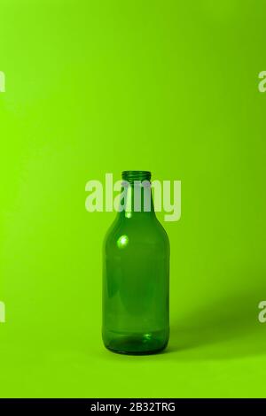 Petite bouteille en verre vert vide sans couvercle et étiquette sur fond vert néon brillant. Peut être utilisé comme maquette pour le jus ou la bière. Banque D'Images