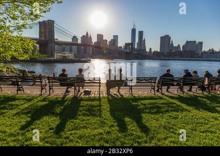 New York, États-Unis CA. Mai 2018: Des personnes assises sur des bancs à New York en regardant le soleil derrière le gratte-ciel de Manhatten Banque D'Images