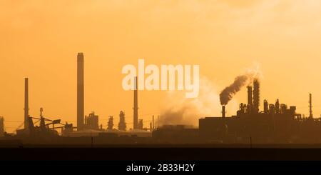 Usine industrielle néerlandaise avec cheminées et moulin à vent au coucher du soleil à Europoort, port de Rotterdam Banque D'Images