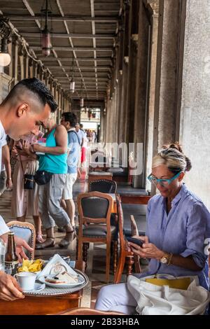 Une femme branchée assise à Caffe Florian, le plus ancien café du monde, Piazza San Marco, Venise, Vénétie, Italie Banque D'Images