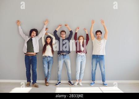 Groupe de jeunes étudiants en vêtements décontractés élevez les mains avec gaieté tout en se tenant sur un fond gris. Banque D'Images