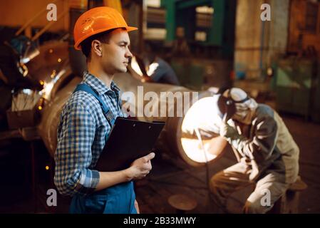 Maître avec ordinateur portable et soudeur en usine Banque D'Images