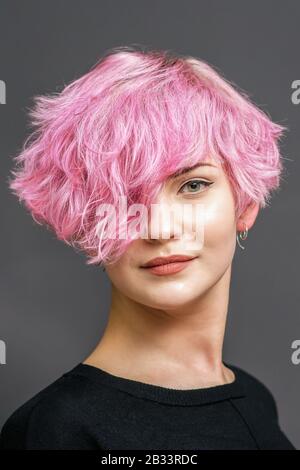 Portrait d'une jeune femme avec nouvelle coiffure rose courte sur fond gris. Banque D'Images