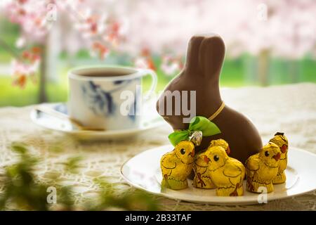 Belle petite table avec décorations de Pâques sur terrasse extérieure. Petit lapin au chocolat avec noeud, œufs au chocolat, tasse de café, bol en cristal. Banque D'Images