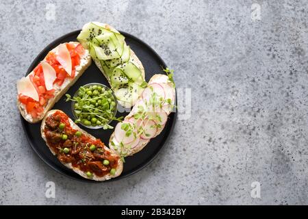 Sandwichs sur toast ciabatta avec légumes frais, radis, tomates, concombres, microgreens de pois décorés sur table en pierre grise. Vue de dessus. Sp Banque D'Images