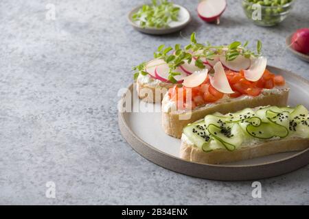 Trois sandwichs sur pain ciabatta avec légumes frais, radis, tomates, concombres et microgreens sur fond gris. Gros plan. Espace de copie. Banque D'Images