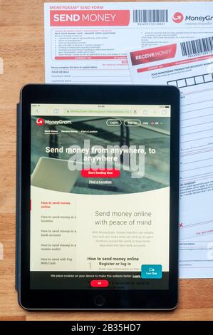 Le site de transfert d'argent moneygram affiché sur une tablette ipad ainsi que des formulaires imprimés pour l'envoi et la réception d'argent. Banque D'Images