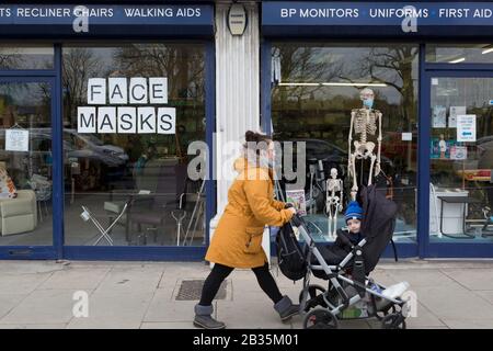 Alors que la pandémie de coronovirus se tient dans tout le Royaume-Uni, 53 cas maintenant signalés par les autorités sanitaires, une mère et un enfant traversent la fenêtre d'une entreprise d'équipements médicaux dans le sud de Londres, affiche un panneau de masques et des masques chirurgicaux sur un mannequin squelette, le 4 mars 2020, À Londres, en Angleterre. Banque D'Images