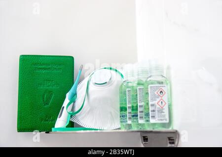 Coronavirus Covid-19 Irlande. Couvercle vert irlandais pour passeport sur étagère à côté du masque respiratoire, des bouteilles de gel désinfectant pour les mains et un thermomètre vert Banque D'Images