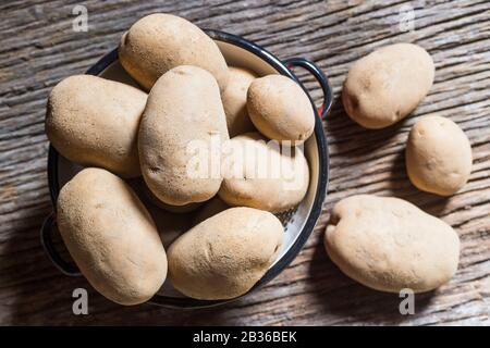 Une pomme de terre dans un drainer sur une vieille planche en bois dans laquelle il y a d'autres pommes de terre. Vue Zenith Banque D'Images