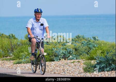 Homme portant un casque à vélo qui longe un pavé de bord de mer au bord de la mer. Cycliste masculin qui monte un vélo au Royaume-Uni. Banque D'Images