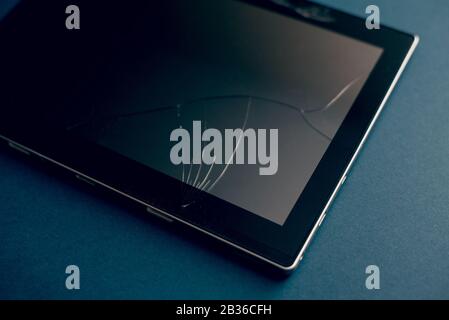Tablette moderne sur fond bleu classique avec fissures. Écran cassé d'une tablette, d'un smartphone ou d'un ordinateur portable. Concept de réparation. Copyspace. Banque D'Images
