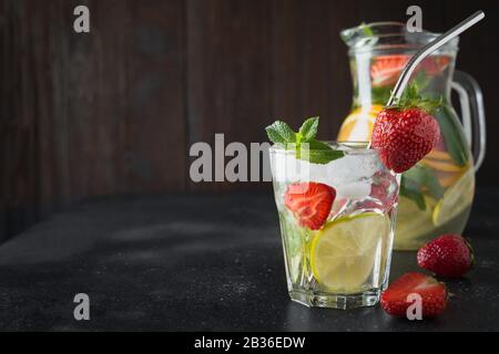 Détox limonade avec citron vert, fraise en verre et pichet isolé sur le panneau sombre. Boisson saine d'été. Vue horizontale. Banque D'Images