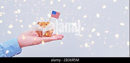 Cupcake avec drapeau américain sur la paume masculine contre fond clair avec des taches colorées. Bannière longue avec espace de copie pour le jour des présidents, le jour du travail, l'indépendance, le drapeau, le jour des anciens combattants, Voter Banque D'Images