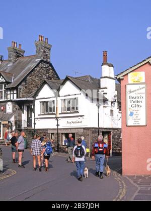 Hawkshead Lake District village dog walking & quelques touristes sac à dos à côté de Beatrix Potter cadeaux inscription personnes dans rue étroite Cumbria England UK Banque D'Images