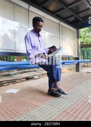 Bangalore, Inde - 17 mai 2019 - un homme indien lit un journal à un arrêt de bus à Bangalore, Inde. Banque D'Images