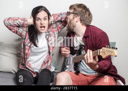 La jeune femme est choquée, ennuyée par le mauvais chant et jouer sa guitare de petit ami et couvrir ses oreilles avec les mains. Banque D'Images