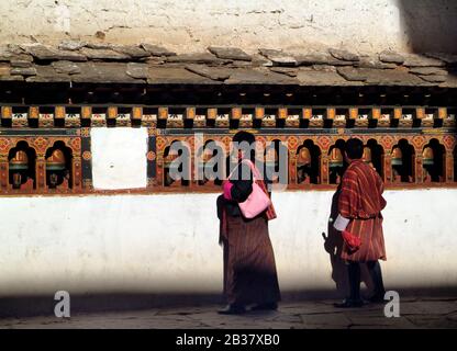 Paro, Bhoutan - 18 septembre 2007: Bhoutanais dans des vêtements traditionnels sur le mur avec des roues de prière à Paro Dzong Banque D'Images