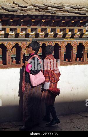 Paro, Bhoutan - 18 septembre 2007: Bhoutanais dans des vêtements traditionnels sur le mur avec des roues de prière à Paro Dzong Banque D'Images