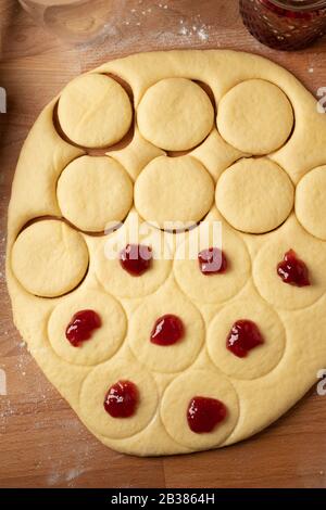 Préparation de beignets faits maison remplis de marmelade de fraises à partir de pâte de levure laminée, vue de dessus Banque D'Images