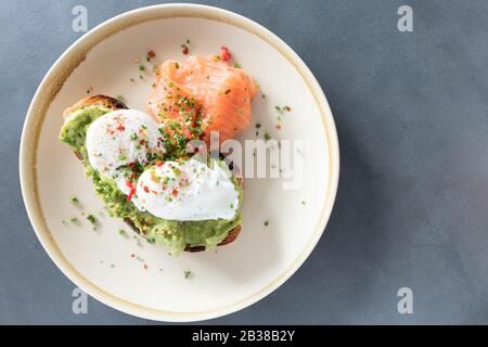 Œufs pochés au-dessus de l'avocat écrasé sur le pain grillé au levain avec du saumon fumé. Petit déjeuner sain avec plaque sur table. Vue de dessus. Copier l'espace vers la droite Banque D'Images