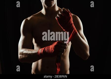 Gros plan sur les mains d'un jeune boxeur qui serpente les bandages rouges avant un match, un combat ou une formation. Banque D'Images